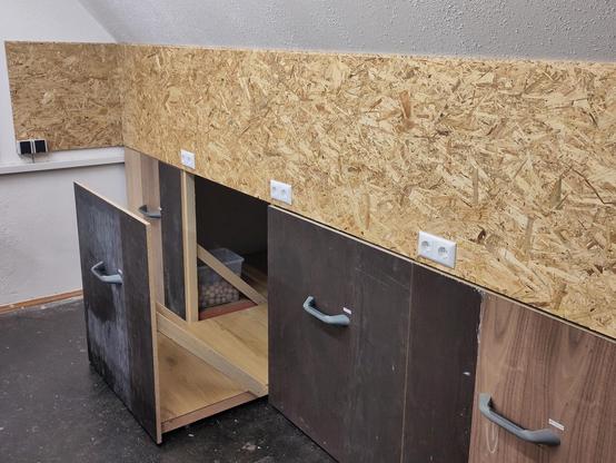 Mehrere Schubladen von der Größe einer Europalette in eine Dachschräge integriert. Eine Schublade ist aufgezogen und gibt den Blick auf die Unterkonstruktion frei.